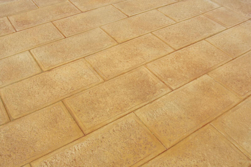 Beige concrete colored by dry granular pigments is stamped with a simple brick pattern