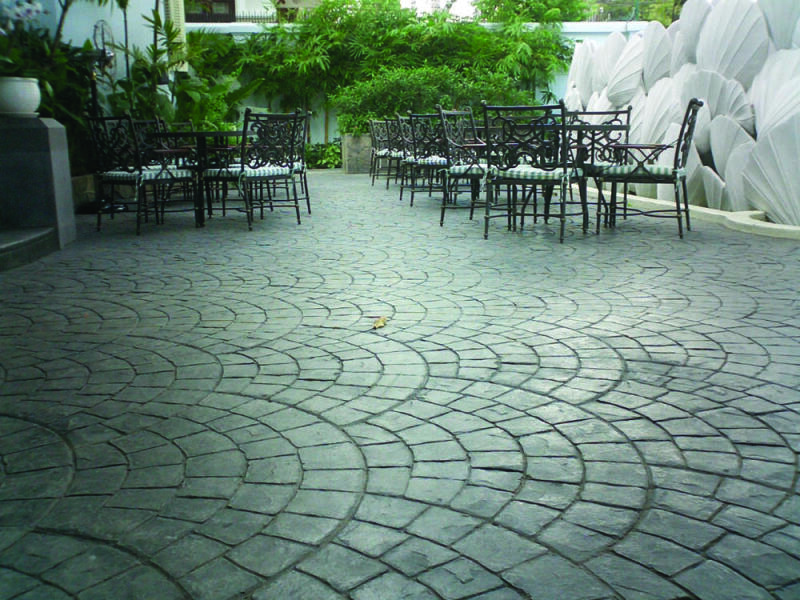 A slate gray concrete large outdoor patio is colored by dry granular pigments and stamped with a mosaic style stone pattern