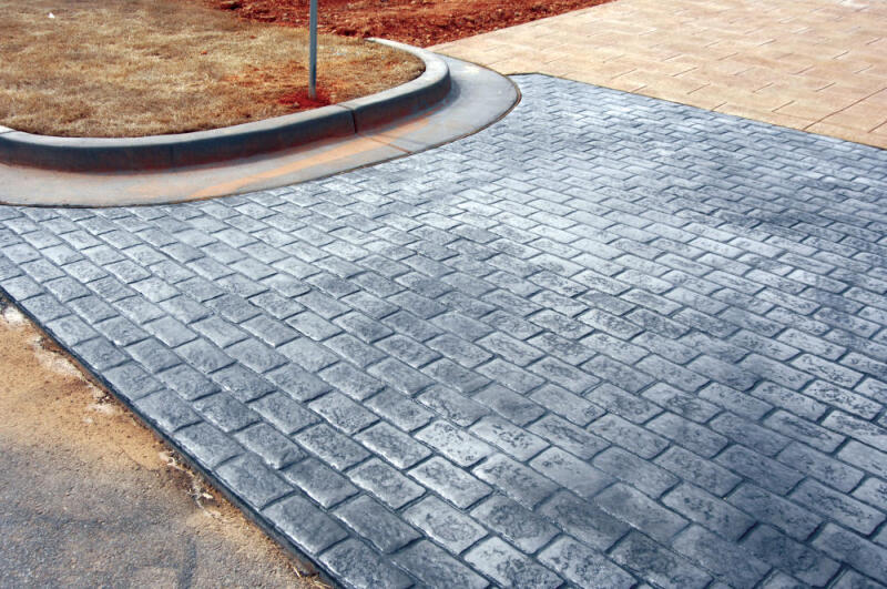 A weathered gray crosswalk is colored by dry granular pigments and stamped with a basic brick pattern