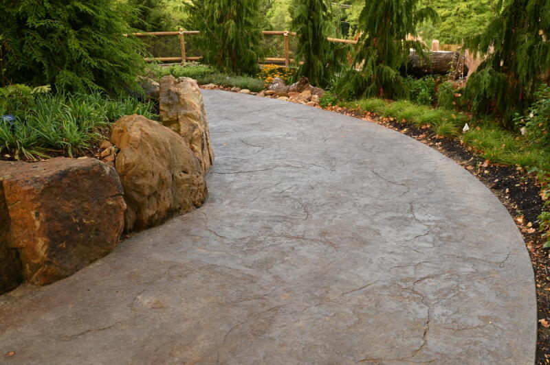 A concrete garden pathway is colored by dry granular pigments and stamped with a textured stone pattern