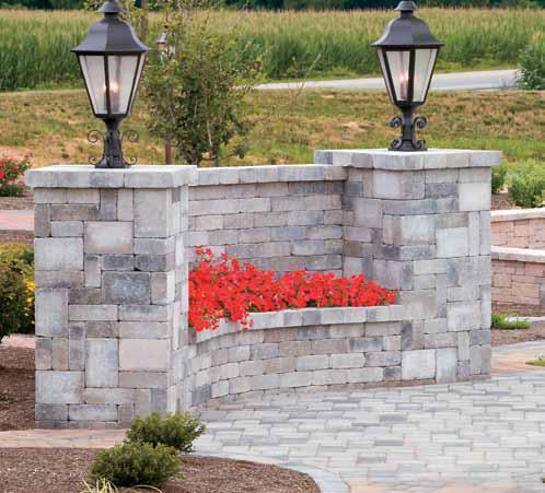 Image of a grey concrete block wall with red flowers and two lamp posts sitting on top of the wall.