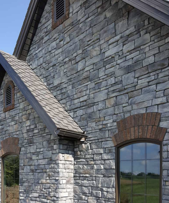 Image of the side of a house that has Provia grey stone wall with brown accent stones around the windows provided by Westview Concrete.